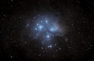 An asterism and open star cluster, with seven prominent stars and several less prominent, surrounded by wisps of blue nebulousity.