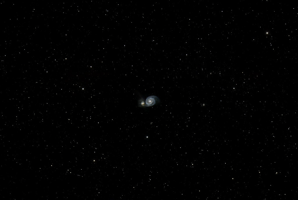 A spiral galaxy in the center of the frame with a smaller galaxy to its left that it is merging with