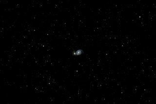 A spiral galaxy in the center of the frame with a smaller galaxy to its left that it is merging with