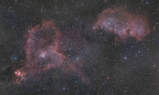 A pair of large diffuse nebulas. One is a ring of red clouds around a cluster at the center that is roughly shaped like a heart, the other an oblong in two parts.