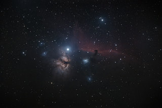 A dark cloud in the shape of a horse’s head set again a lane of red dust, with a bright start to its left. Below that bright star in the frame is the Flame Nebula, dark tendrils against a light orange/brown cloud reminiscent of flame.