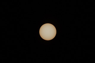 The sun, full and yellow, in the center of the frame, with a small, black sunspot on its upper right quarter.