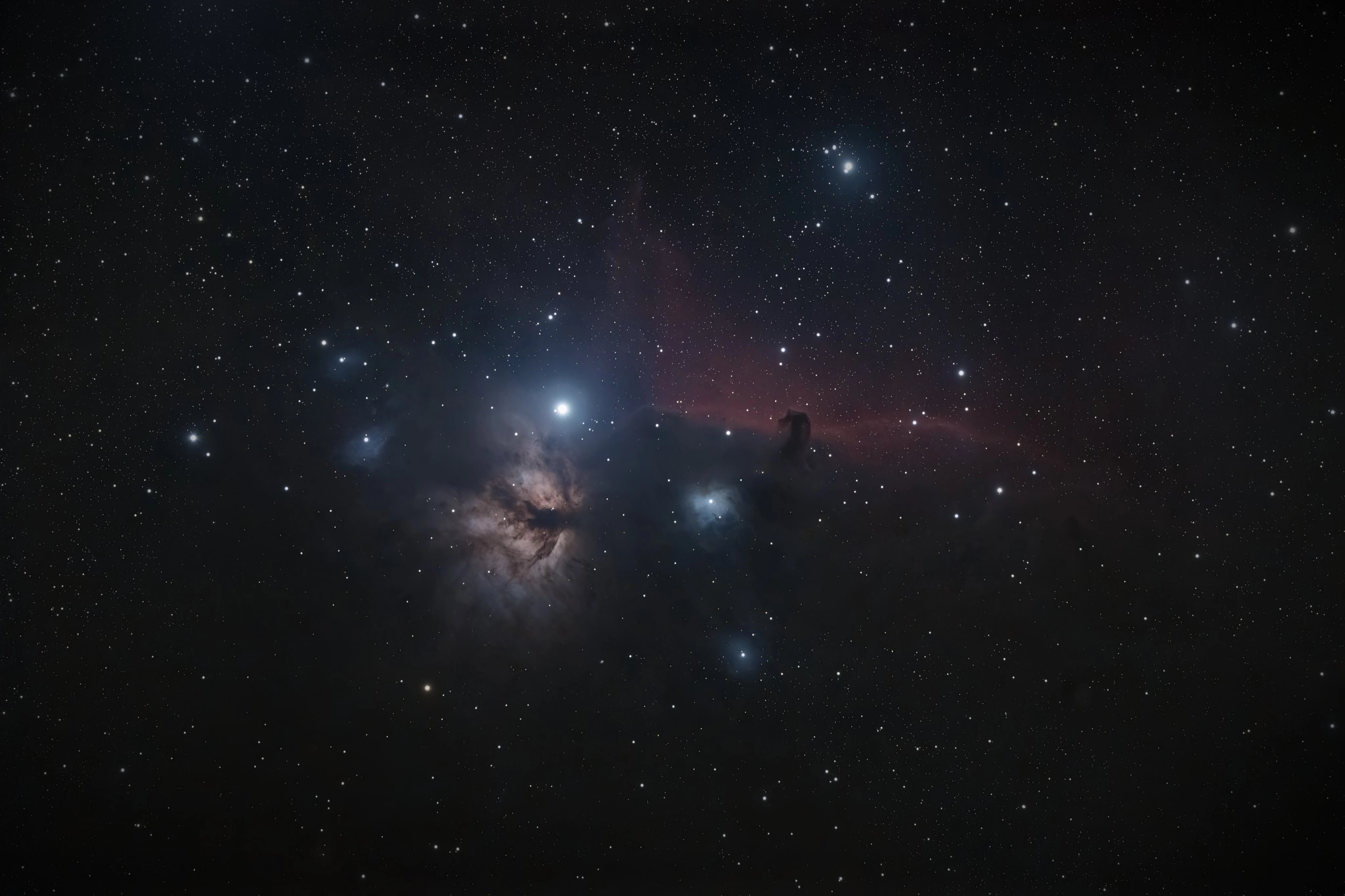 A dark cloud in the shape of a horse’s head set again a lane of red dust, with a bright start to its left. Below that bright star in the frame is the Flame Nebula, dark tendrils against a light orange/brown cloud reminiscent of flame.